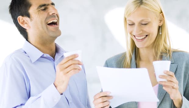 Businessman and businesswoman holding cups and laughing over document