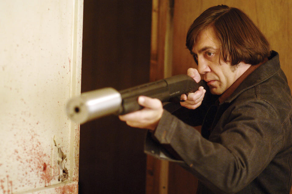 Javier Bardem points a makeshift shotgun at someone; blood is on the walls