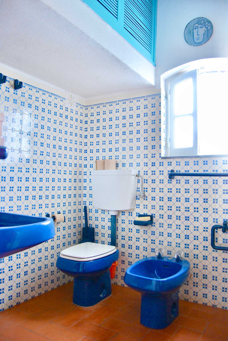 Blue toilet, bidet, and sink in bathroom with blue and while tiling.