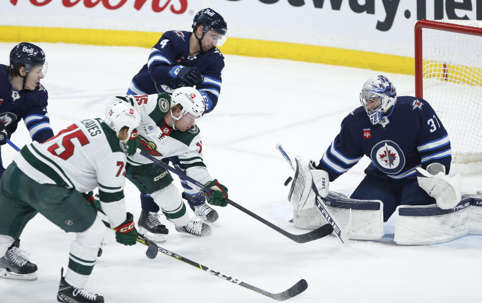 Winnipeg Jets goaltender Connor Hellebuyck (37) saves the shot by Minnesota Wild's Mason Shaw (15) as Logan Stanley (64) and Neal Pionk (4) defend during the second period of an NHL hockey game, Wednesday, March 8, 2023 in Winnipeg, Manitoba. (John Woods/The Canadian Press via AP)