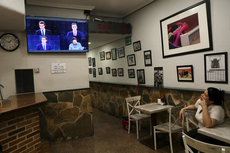 Perla, a worker at a bar, takes a break from cleaning to watch candidates for Spanish general elections People's Party (PP) Pablo Casado, Spanish Prime Minister and Socialist Workers' Party (PSOE) Pedro Sanchez, Ciudadanos' Albert Rivera and Unidas Podemos' Pablo Iglesias on a television screen during a live televised debate ahead of general elections in Madrid, Spain, April 22, 2019. REUTERS/Susana Vera