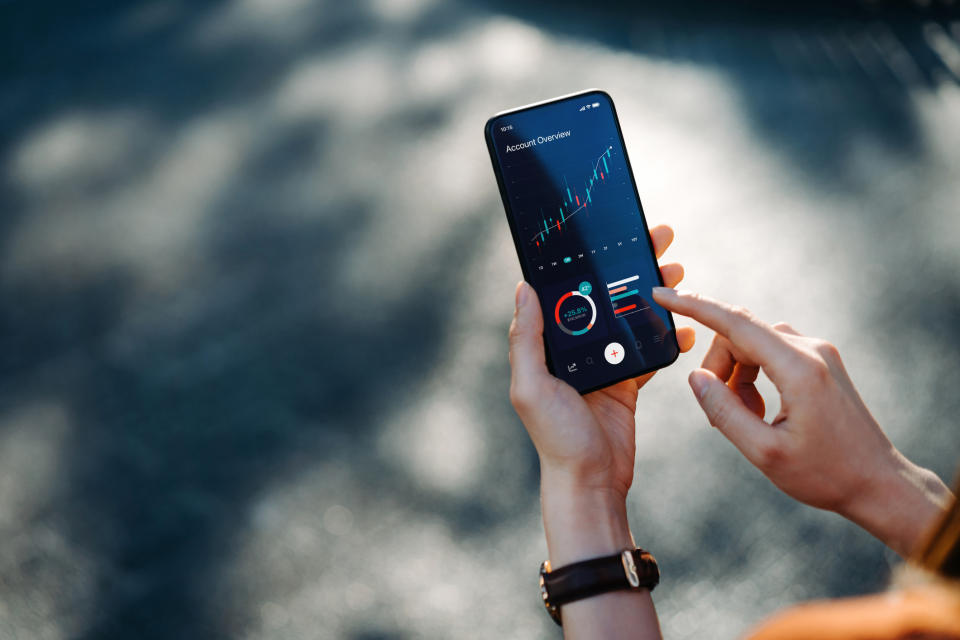 A person using a smartphone to view financial graphs and data, focusing on a chart with rising trends