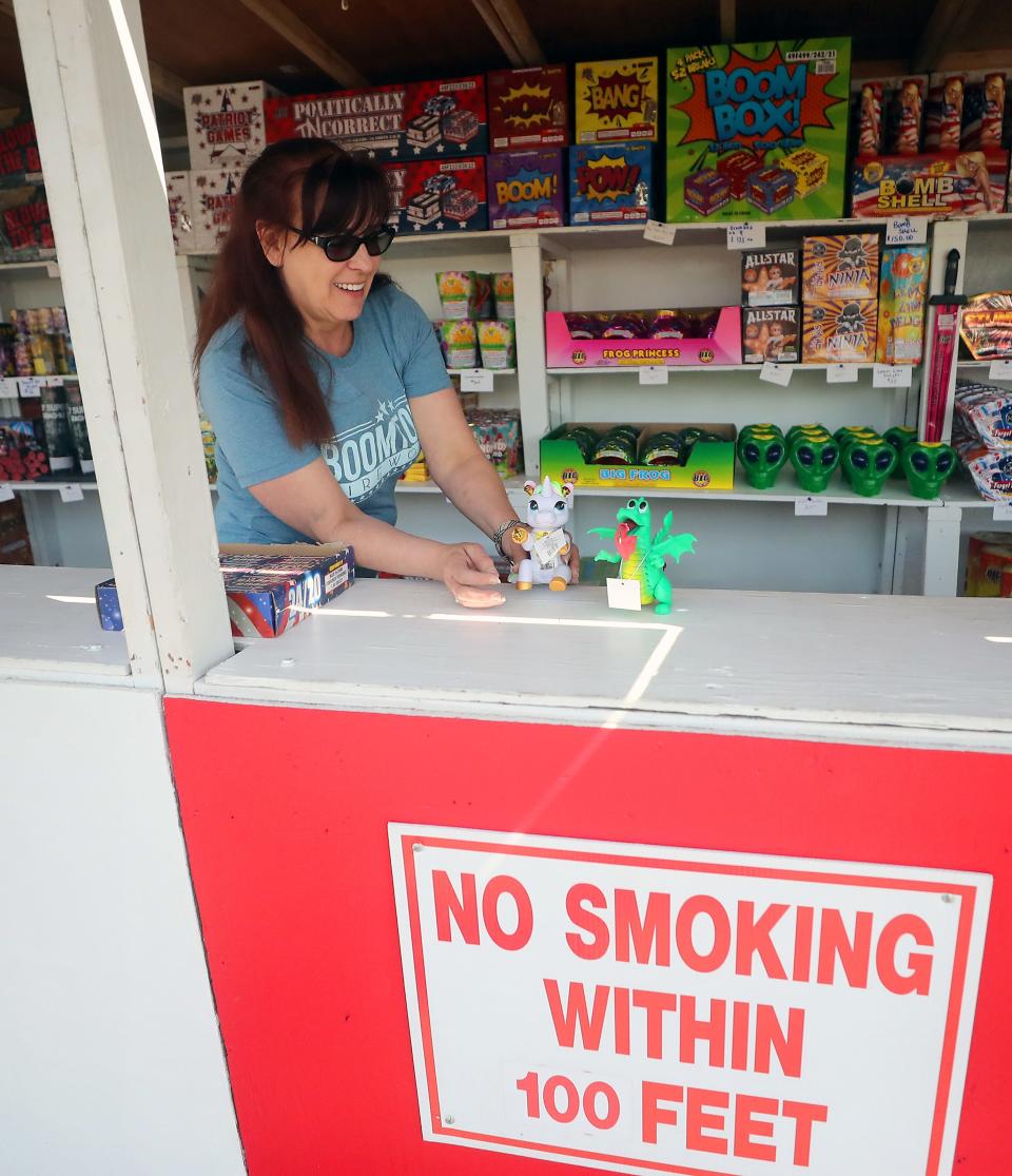 Kimberly Duncan shows off a pair of dragon and unicorn-shaped fireworks while working in the Boomtown Fireworks stand in East Bremerton on Thursday.