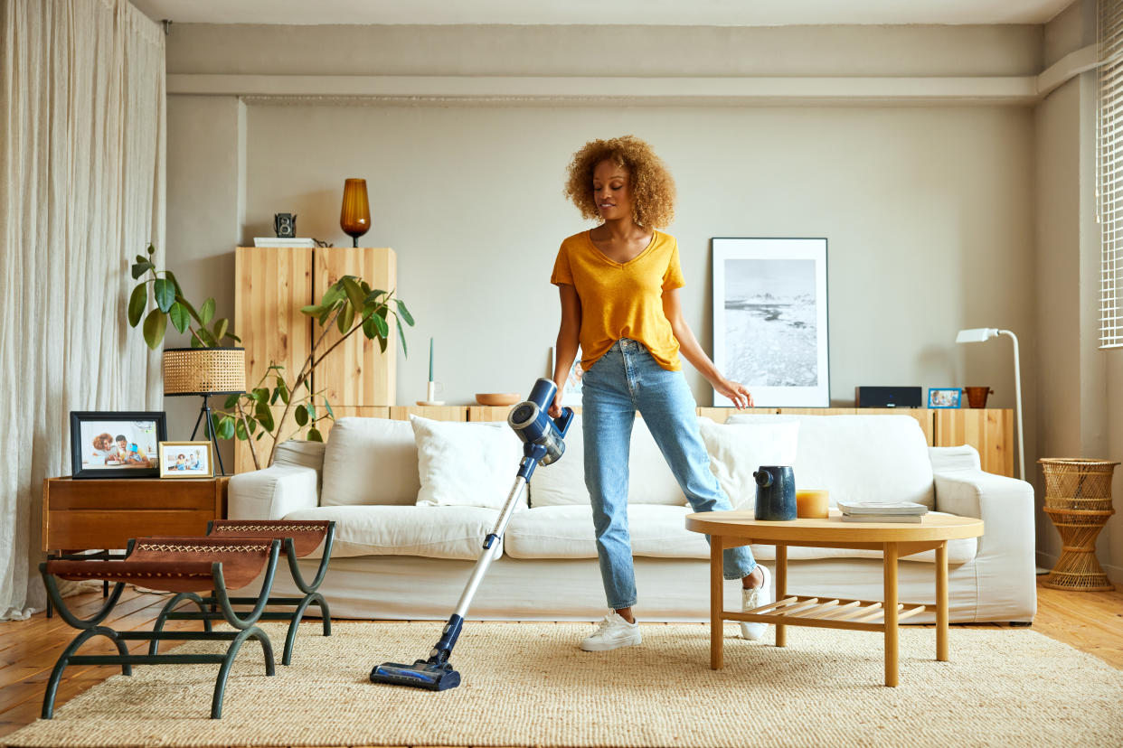 Prime day vacuum deal woman in orange t-shirt and jeans vacuuming home in front of white couch and carpet, cordless vacuum cleaner sale amazon canada