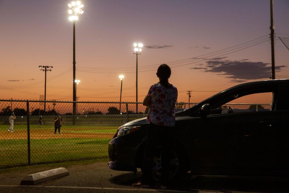 A woman watches youth play baseball near Kennedy Middle School in El Centro, Calif., on July 7, 2021. The City of El Centro consistently ranks as having the highest unemployment rate in the country.
