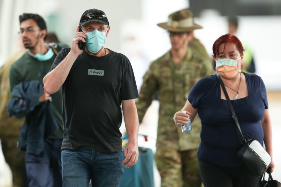 Returning overseas travellers walk towards waiting buses at Sydney Airport.