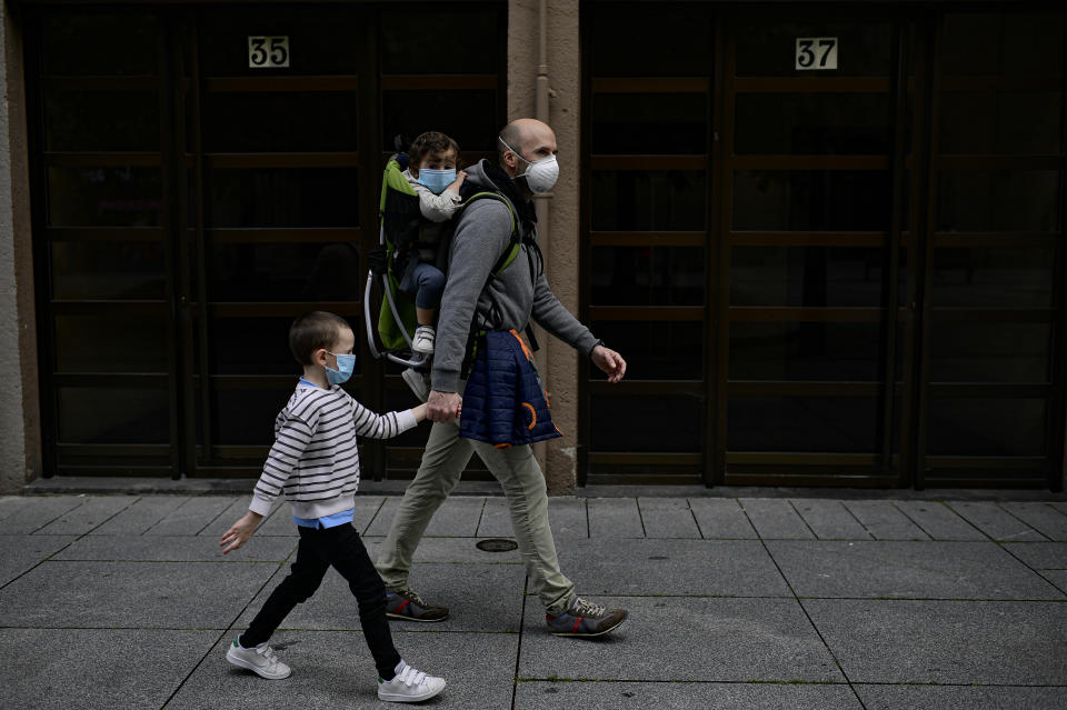 A father with his children wearing face mask to prevent the coronavirus go for a walk at Carlos III promenade, in Pamplona, northern Spain, Sunday, April 27, 2020. On Sunday, children under 14 years old will be allowed to take walks with a parent for up to one hour and within one kilometer from home, ending six weeks of compete seclusion. (AP Photo/Alvaro Barrientos)
