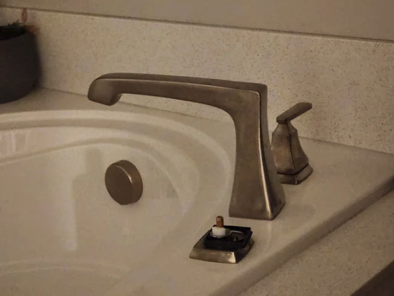 Bathroom sink with a broken faucet handle. The handle is detached from its base, revealing internal parts