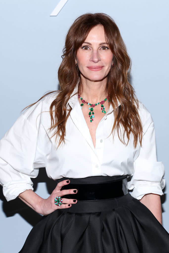 Julia Roberts posing in a white blouse and black skirt adorned with a green stone necklace and ring