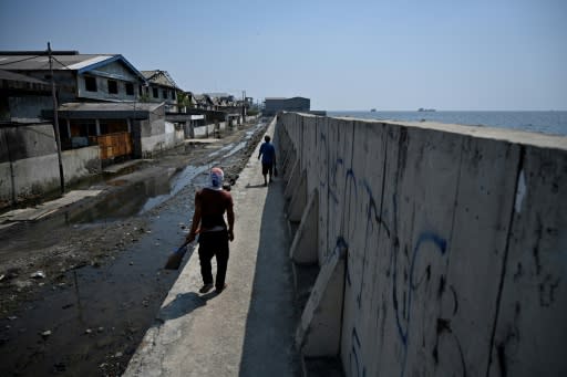 A man walks on a giant sea wall to avoid a flooded road next to abandoned warehouses in northern Jakarta