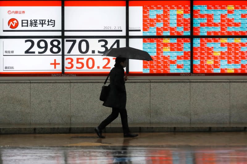 FILE PHOTO: A man holding an umbrella walks in front of an electric board showing Nikkei index at a brokerage in Tokyo