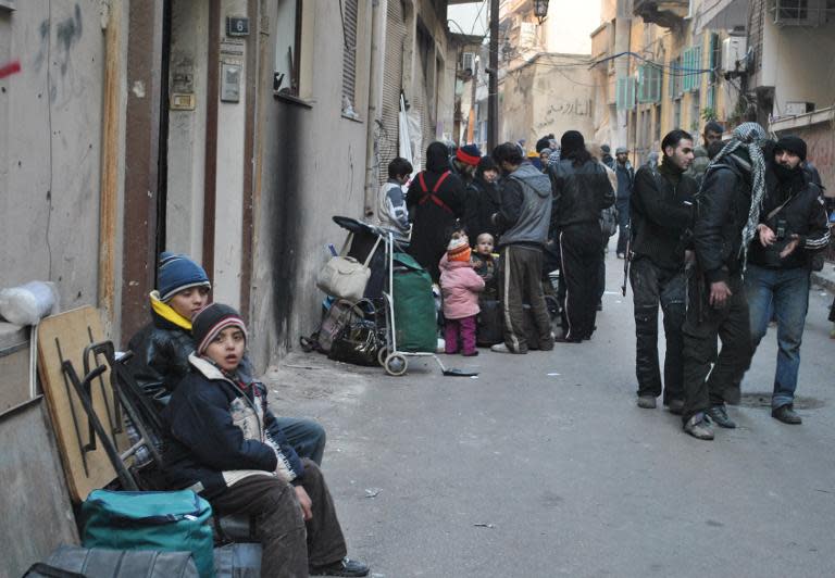 Syrians gather with their belongings in a street in Homs on February 8, 2014 as a UN and Red Crescent humanitarian convoy delivers food and medical aid