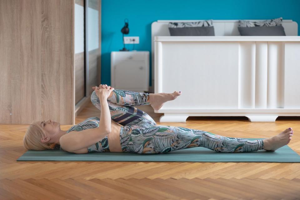 woman lying on mat at home and stretching leg bent in knee to chest