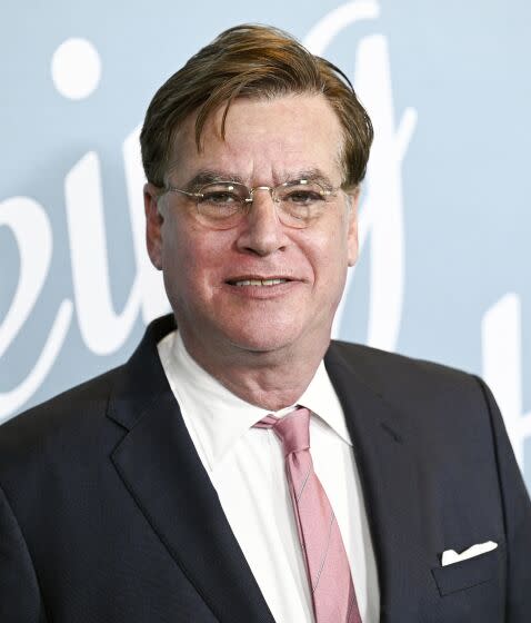 A man with glasses in a black blazer, white shirt and pink tie smiles