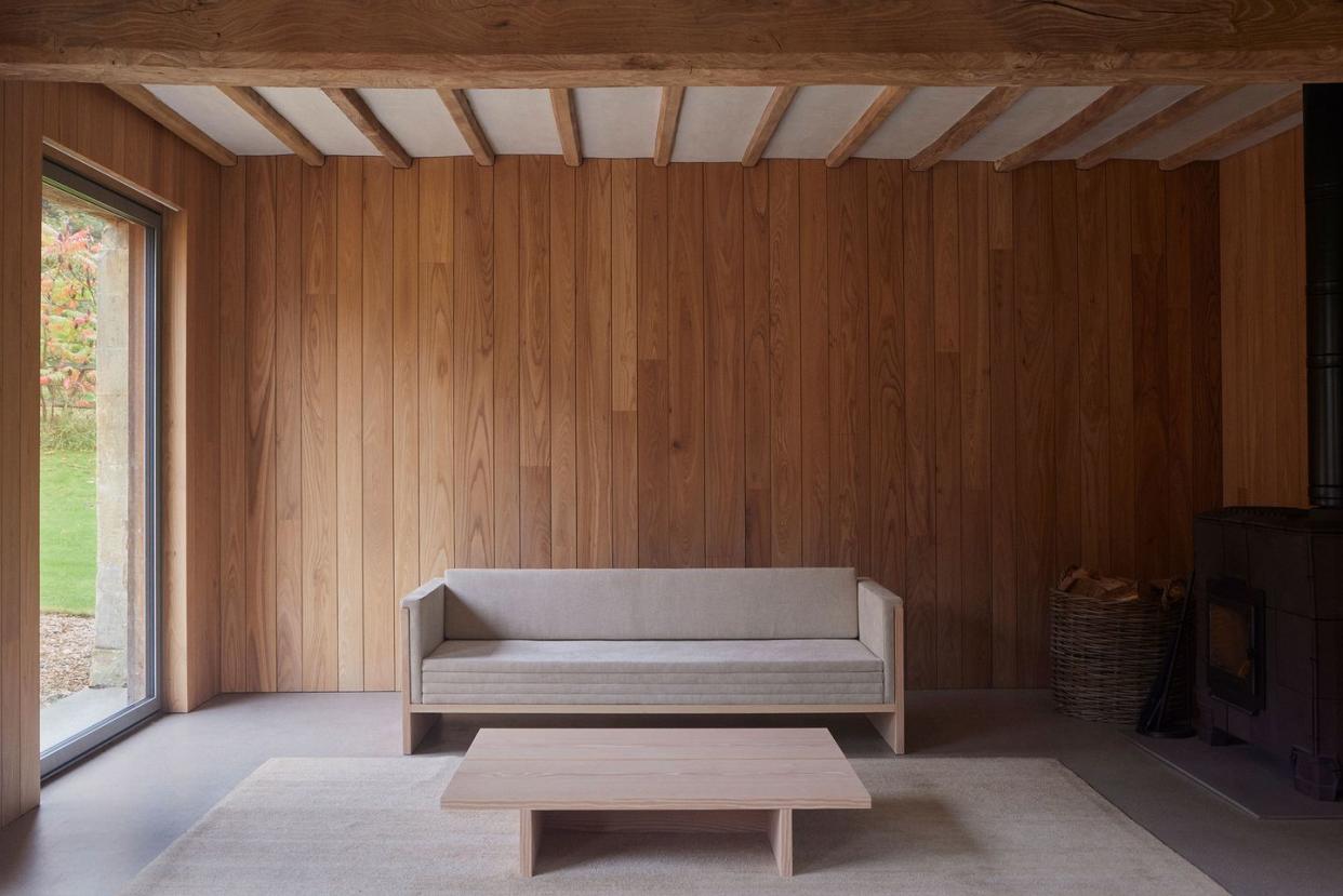 long wood daybed in simple elegant lines with velvet cushions and a simple matching cocktail table all against a panelled honey colored wall