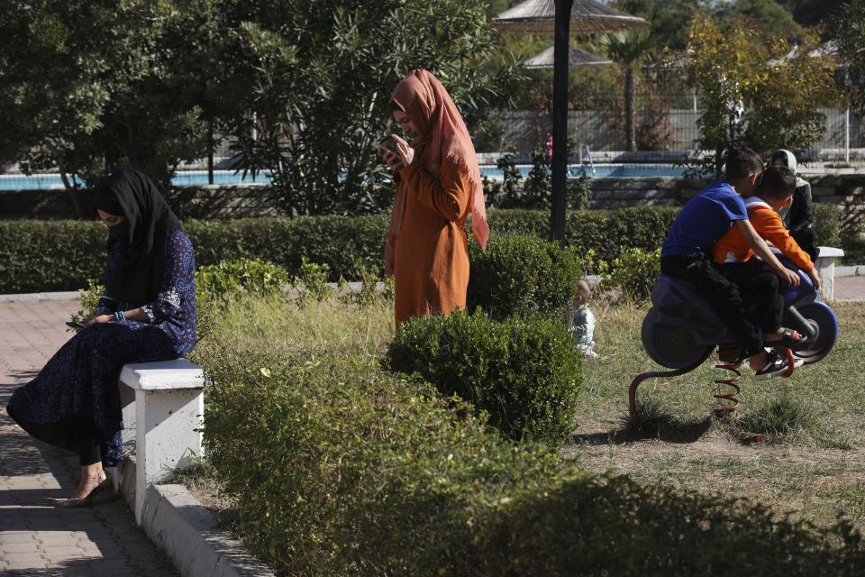 Afghan women look at their cell phones as children play at a coastline tourist resort of Golem, 50 kilometers (30 miles) west of Tirana, Albania, Wednesday, Oct. 27, 2021. A group of Afghans evacuated earlier this month are housed at an Albanian coastline tourist resort enjoying the warm welcome and a normal daily life. The last group of judges, sportsmen, journalists, activists, artists, law enforcement officers, scientists and more arrived earlier in October. They all miss and fear of the fate of their families back home. (AP Photo/Franc Zhurda)