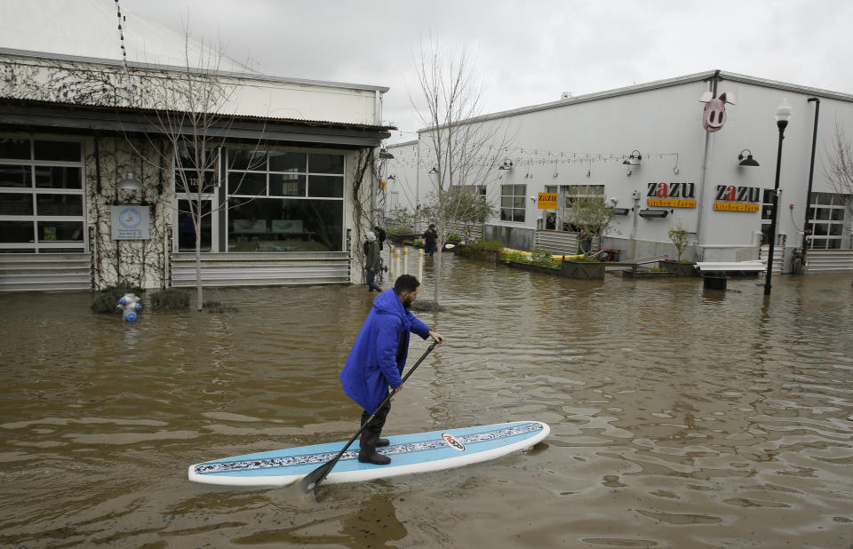 A man uses a paddle board to make his way through the flooded Barlow Market District Wednesday, February 27, 2019, in Sebastopol, California.&nbsp;