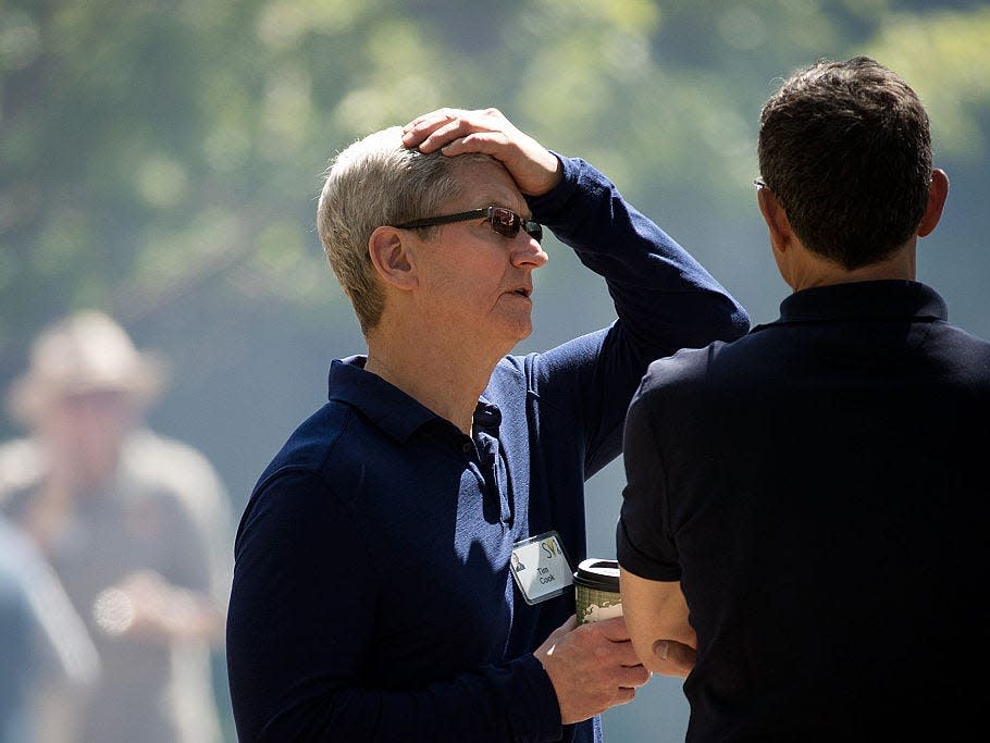 Tim Cook talking to someone with one hand on his head and one holding a coffee cup.