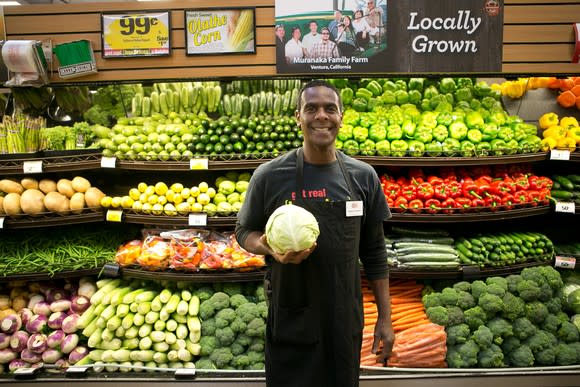 Worker in produce aisle holding a head of lettuce.