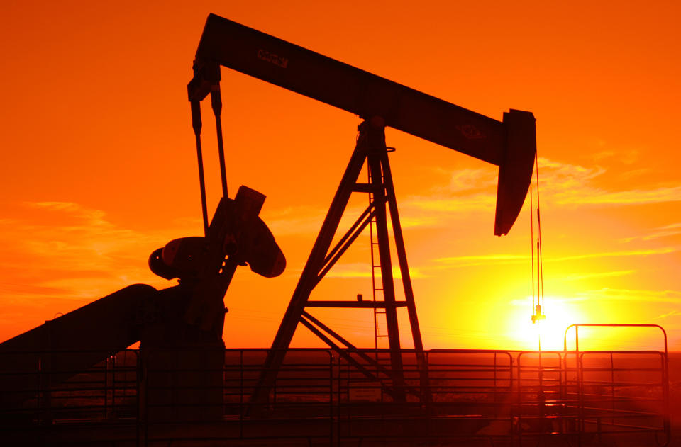 An oil pump jack with an orange sunset in the background.