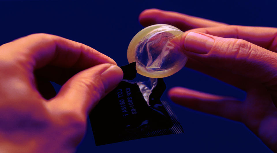 Two hands holding an unwrapped condom, preparation for safe sex practice