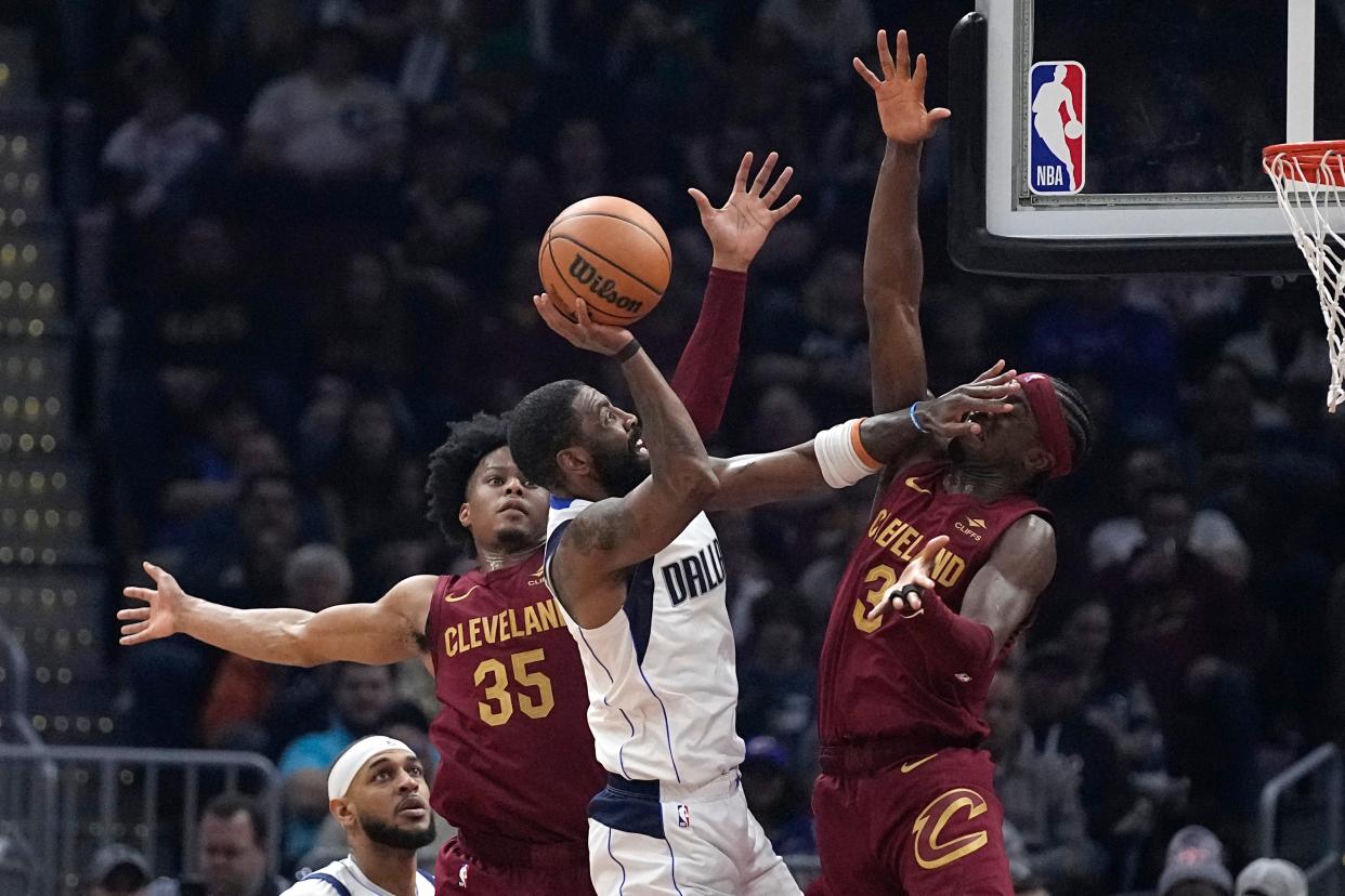 Mavericks guard Kyrie Irving, center, shoots from between Cavaliers forward Isaac Okoro (35) and guard Caris LeVert (3) during the first half, Tuesday, Feb. 27, 2024, in Cleveland.
