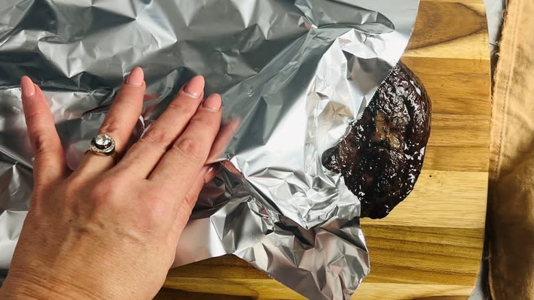 hand putting foil on steak on cutting board