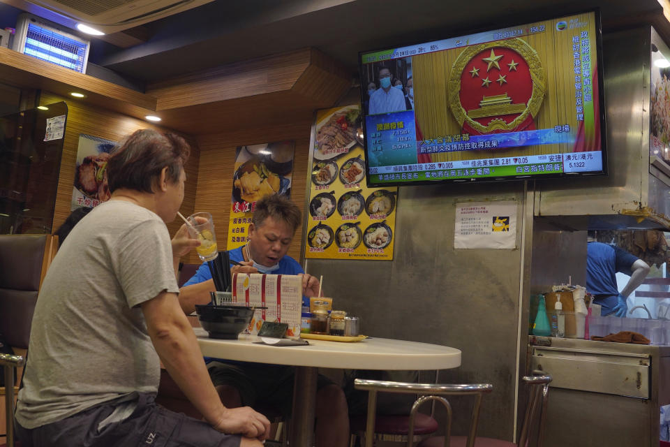 People have lunch beneath a television showing live telecast of the closing session of the National People's Congress, in Hong Kong, Thursday, May 28, 2020. China’s ceremonial legislature on Thursday endorsed a national security law for Hong Kong that has strained relations with the United States and Britain. (AP Photo/Vincent Yu)