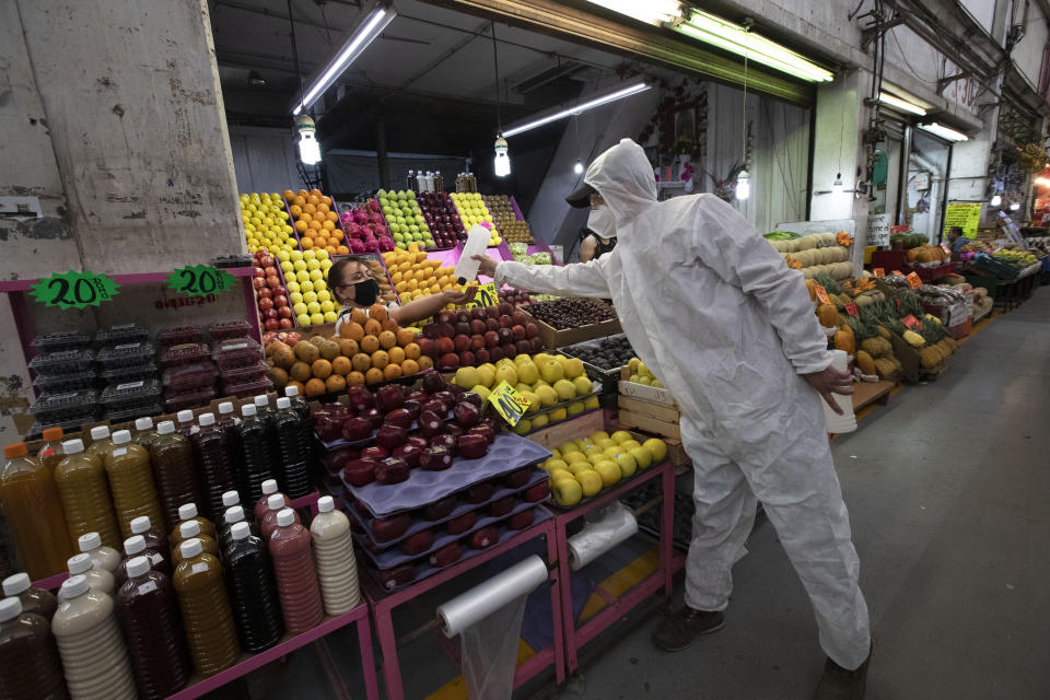 A health worker in protection gear as a measure to curb the spread of the new coronavirus, gives alcohol to a vendor to disinfect her hands at the Central de Abasto market in Mexico City, Thursday, June 18, 2020. The passageways at the market have remained crowded despite the pandemic. (AP Photo/Marco Ugarte)