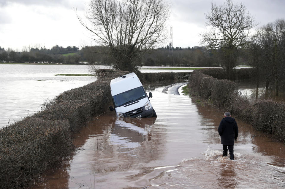 A man makes his through floodwater past an abandoned vehicle near the village of Hampton Bishop near Hereford, after the River Lugg burst its banks, Wales, Tuesday Feb. 18, 2020. Britain's Environment Agency issued severe flood warnings Monday, advising of life-threatening danger after Storm Dennis dumped weeks' worth of rain in some places. (Steve Parsons/PA via AP)