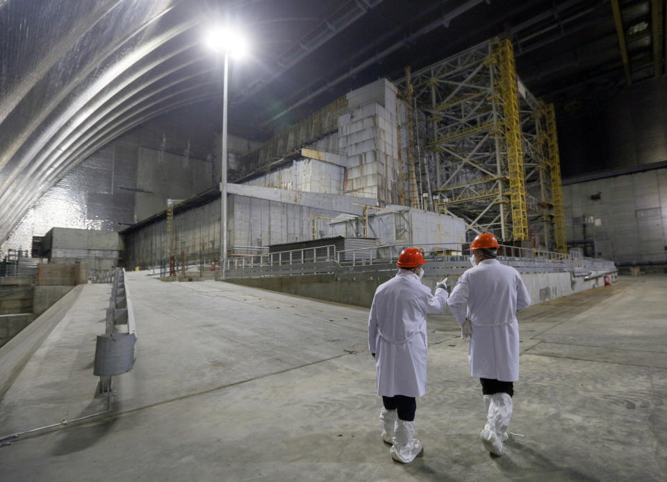 Workers walk past the covered exploded reactor inside a shelter construction at the Chernobyl nuclear plant, in Chernobyl, Ukraine, Thursday, April 15, 2021. The vast and empty Chernobyl Exclusion Zone around the site of the world’s worst nuclear accident is a baleful monument to human mistakes. Yet 35 years after a power plant reactor exploded, Ukrainians also look to it for inspiration, solace and income. (AP Photo/Efrem Lukatsky)