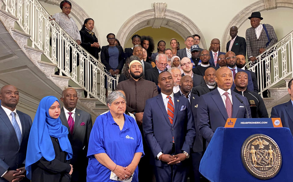 New York City Mayor Eric Adams surrounded by constituents including a woman in a hijab and a man in a white pillbox cap.