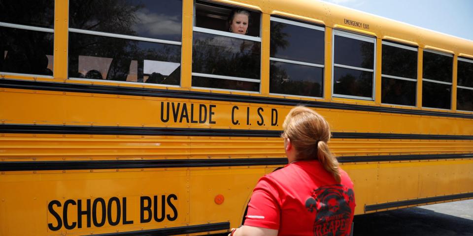 A school employee talking through the window of a school bus to a parent at Robb Elementary School.