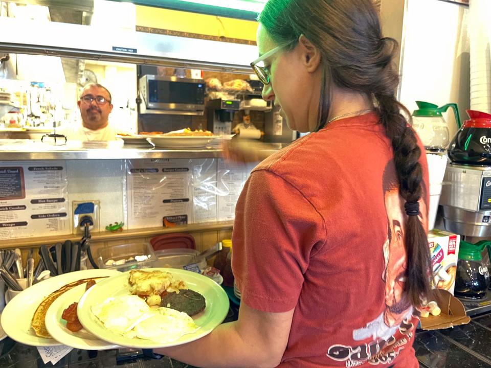 Owner Sam looks on as Felicia Ritter expertly loads up her arms with breakfast dishes at Sami’s Café, 9700 Kingston Pike, Tuesday, July 5, 2022.