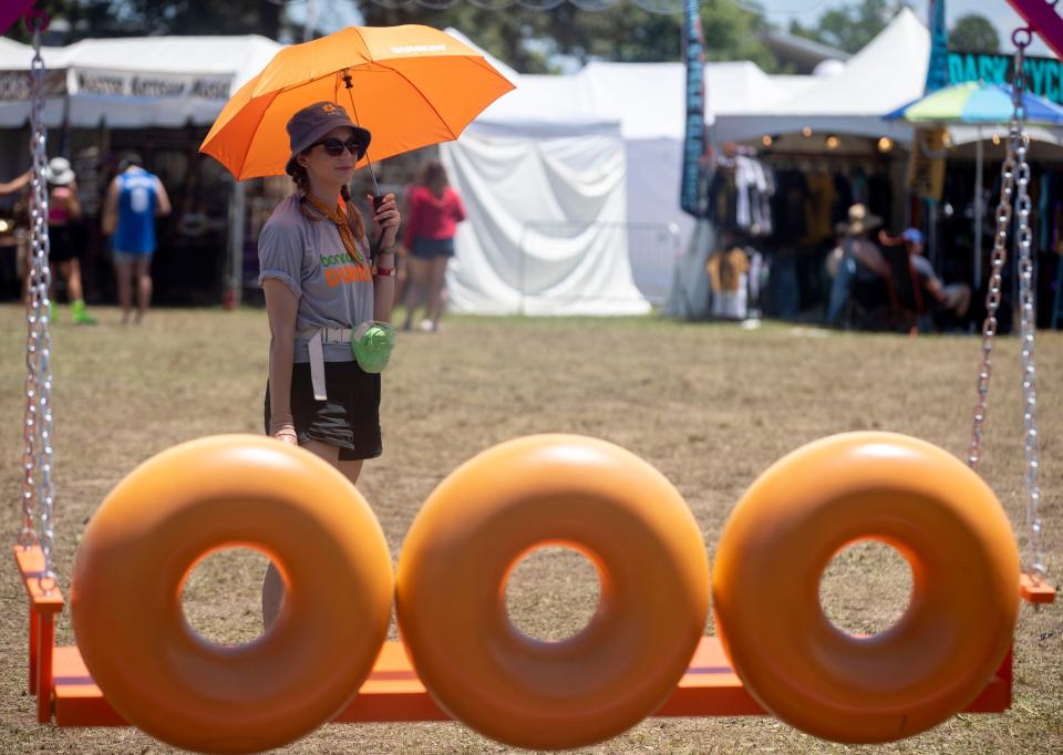 Courtney Gates stands in the shade of her umbrella at the Dunkin' Donuts booth during the third day of Bonnaroo on Saturday, June 18, 2022, in Manchester, Tenn. 