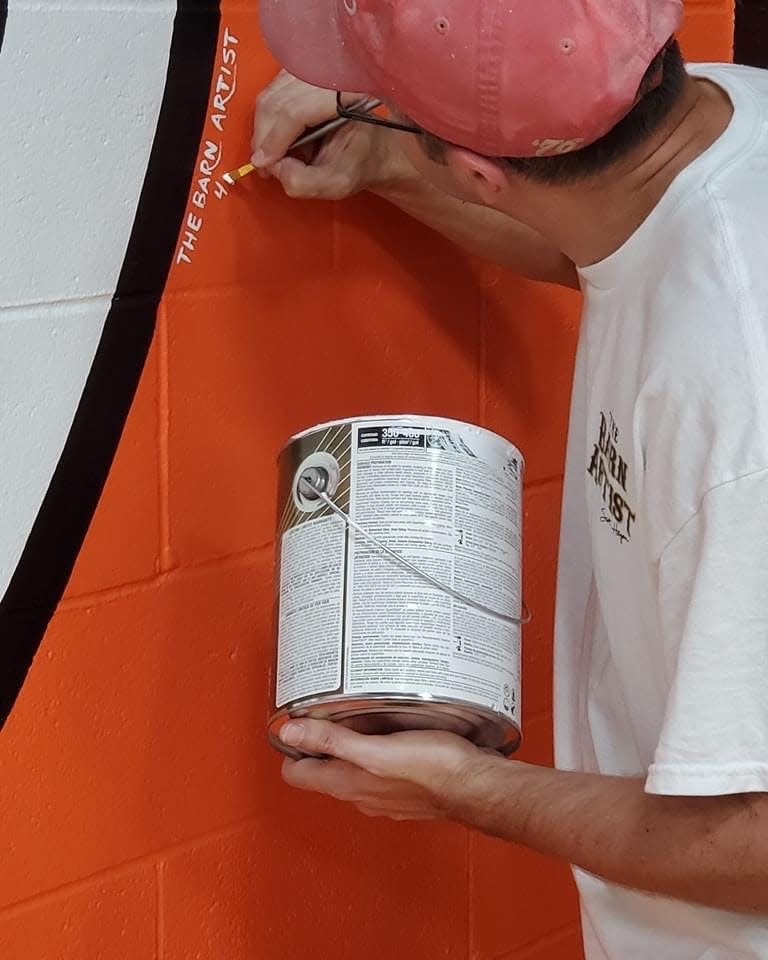 Scott Hagan, who's known as "The Barn Artist," signs his name to a mural he painted at Newcomerstown High School.