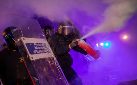A policeman uses a fire extinguisher on a burning barricade during clashes - Credit: Bernat Armangue/AP