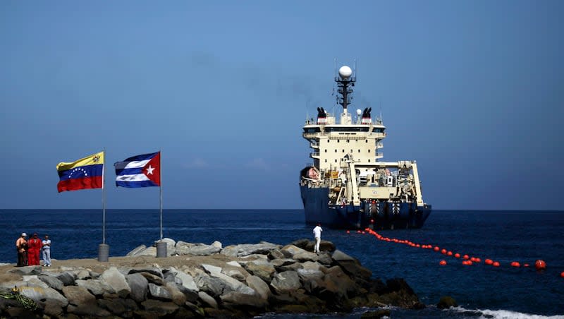 In this Jan. 22, 2011, file photo, people stand on a breakwater, with a Venezuelan flag, left, and a Cuban flag as a specialized ship rolls out a fiber-optic cable, suspended from buoys, off La Guaira, Venezuelan coast.
