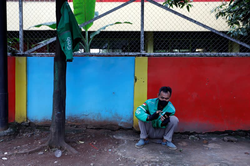 An online motorbike taxi driver uses his smartphone while waiting for customers in Jakarta