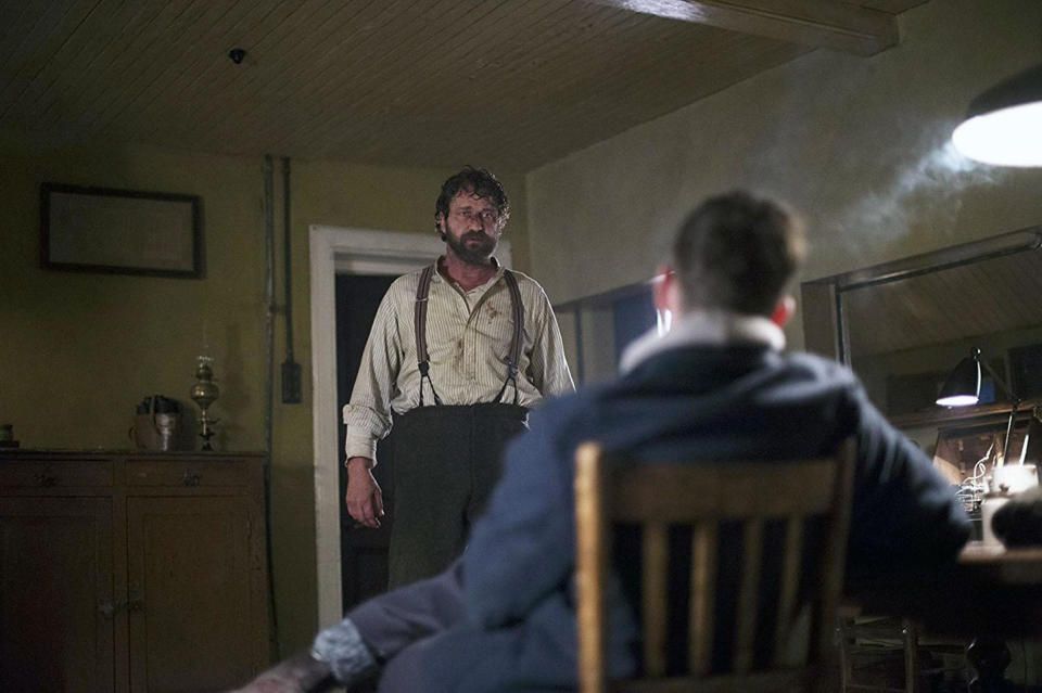 A bruised and bloodied man in suspenders confronts someone in a smokey room