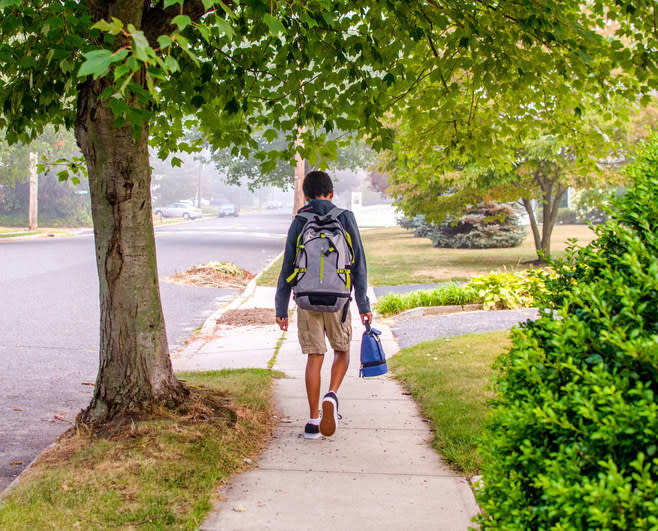 A kid walking on the sidewalk with their backpack and lunchbox