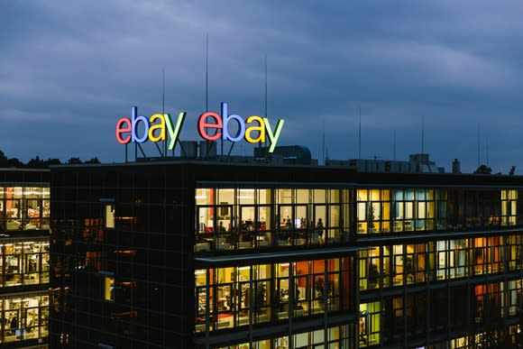Office building with lights turned on under a dark sky with the eBay logo displayed on the roof of the building.