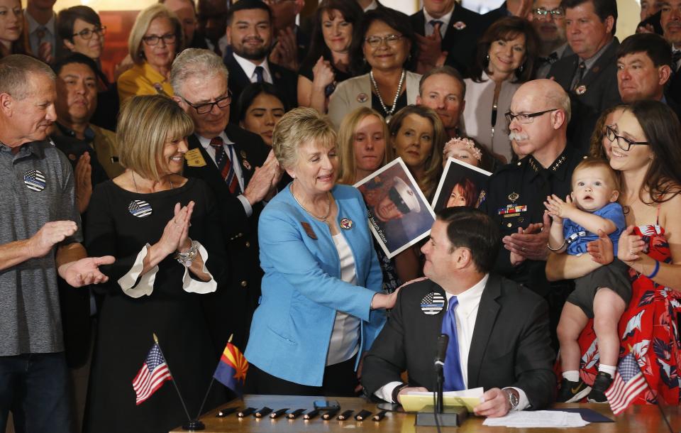 Arizona Republican Gov. Doug Ducey, seated, smiles as he gets a pat on the shoulder from bill sponsor Sen. Kate Brophy McGee, third from left, R-Phoenix, as the governor signs into law a distracted driving bill during a ceremony at the Arizona Capitol Monday, April 22, 2019, in Phoenix. Arizona becomes the 48th state to ban texting and the 18th to ban any hand-held phone use while driving. Officers can begin issuing warnings immediately and can write tickets in 2021. (AP Photo/Ross D. Franklin)