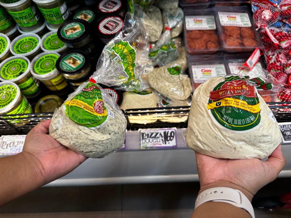 two hands holding bags of premade pizza dough at trader joes