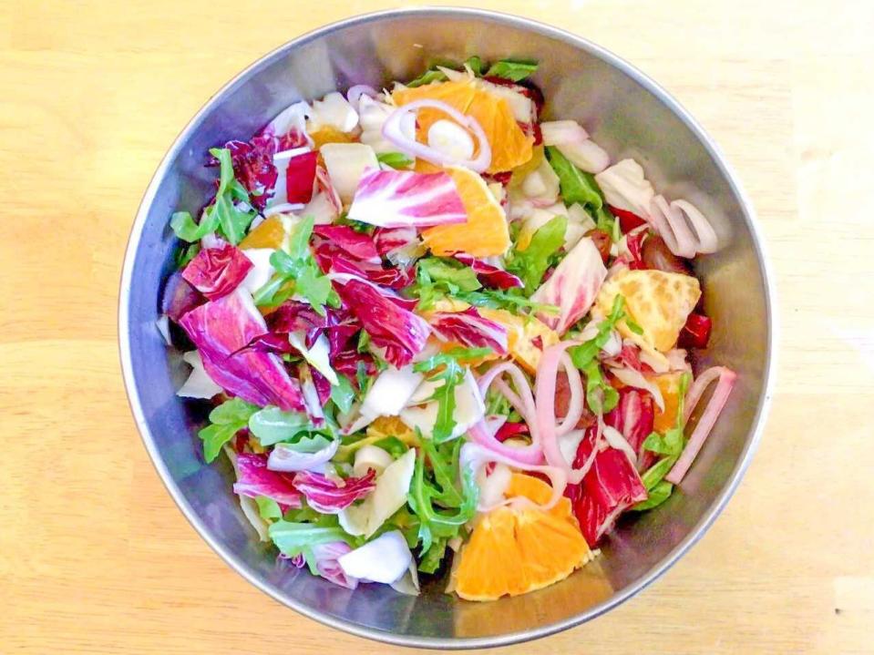 Bird's-eye-view of a bowl of salad holding arugula, oranges, red cabbage, and olives