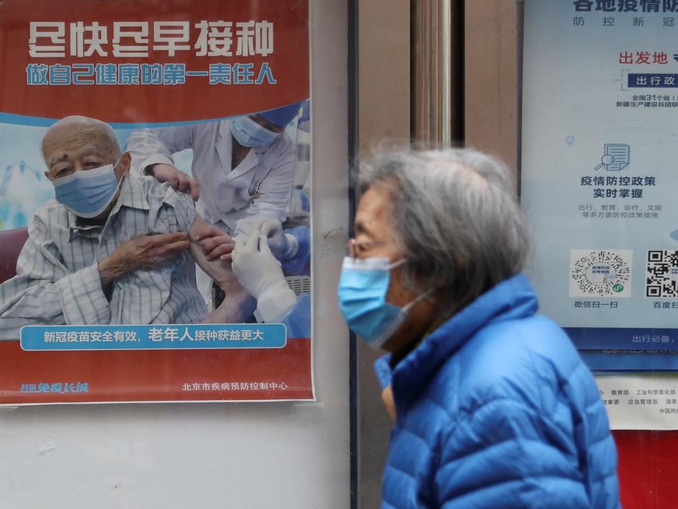 person with grey hair walks past poster of an older man getting vaccinated
