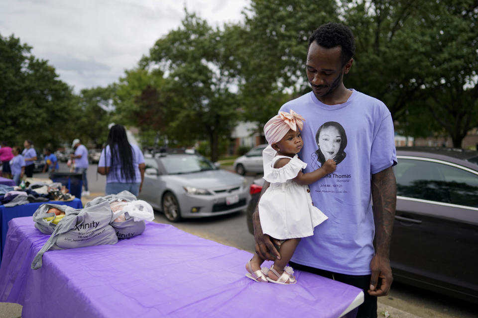 Denver Mundle looks to his baby daughter Nevaeh Mundle as she holds his T-shirt with an image of his cousin Nikiesha Thomas during a Back To School Block Party in the Robinwood Community of Annapolis, Md., Sunday, Aug. 21, 2022, in honor of Thomas. The block party was hosted by Beacon Light Seventh-day Adventist Church, and sponsored by the Nikiesha Thomas Memorial and Allstate Insurance. Thomas was shot and killed by her ex-boyfriend just days after filing for a protective order. (AP Photo/Carolyn Kaster)