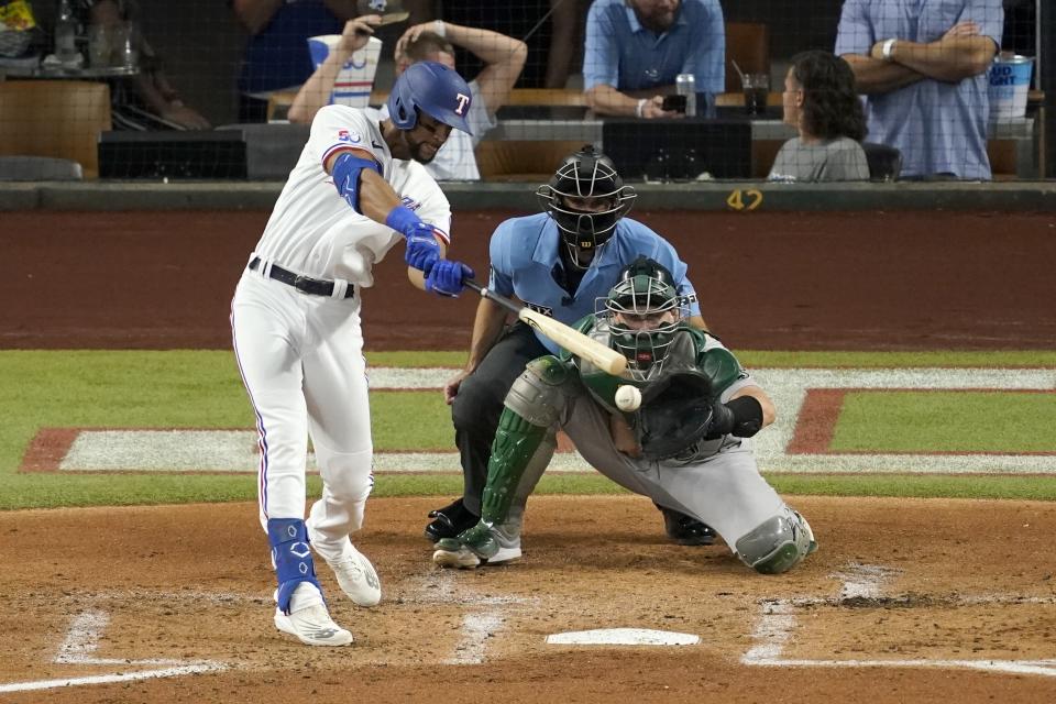 Texas Rangers' Leody Taveras connects for a two-run single in the first inning of a baseball game as Oakland Athletics catcher Sean Murphy and umpire John Tumpane look on, Wednesday, July 13, 2022, in Arlington, Texas. (AP Photo/Tony Gutierrez)
