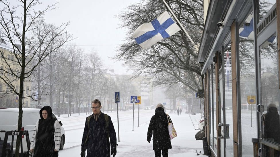 Pedestrians walk under a flag flying at half-mast during a day of mourning after a school shooting in Helsinki