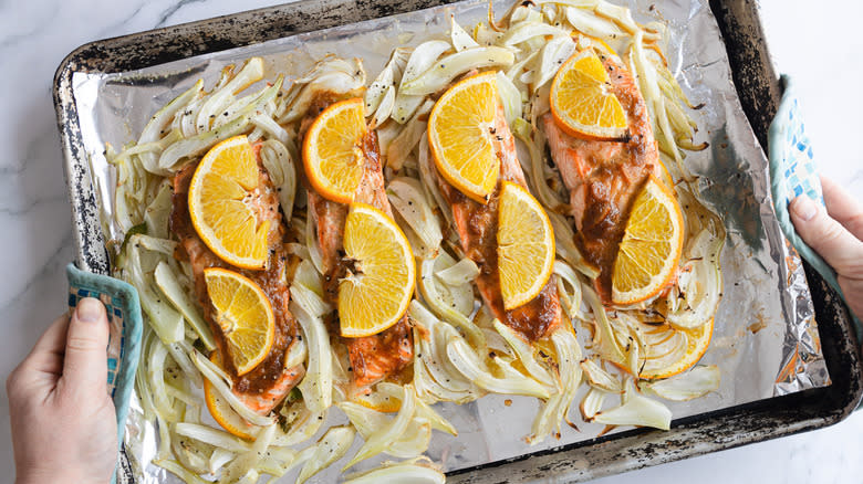 hands holding  baked salmon on sheet